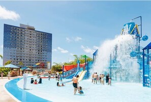 Parque acuático con una piscina grande, toboganes y una fuente de agua alta.