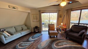 A living room with a sofa, armchairs, a coffee table, and a rug. There is a ceiling fan, a window with a view of trees, and a sign that reads "Welcome to Lake". - Lakefront Aframe Cabin in Hardy on Kiwanie Lake with kayaks and private dock (Hardy)