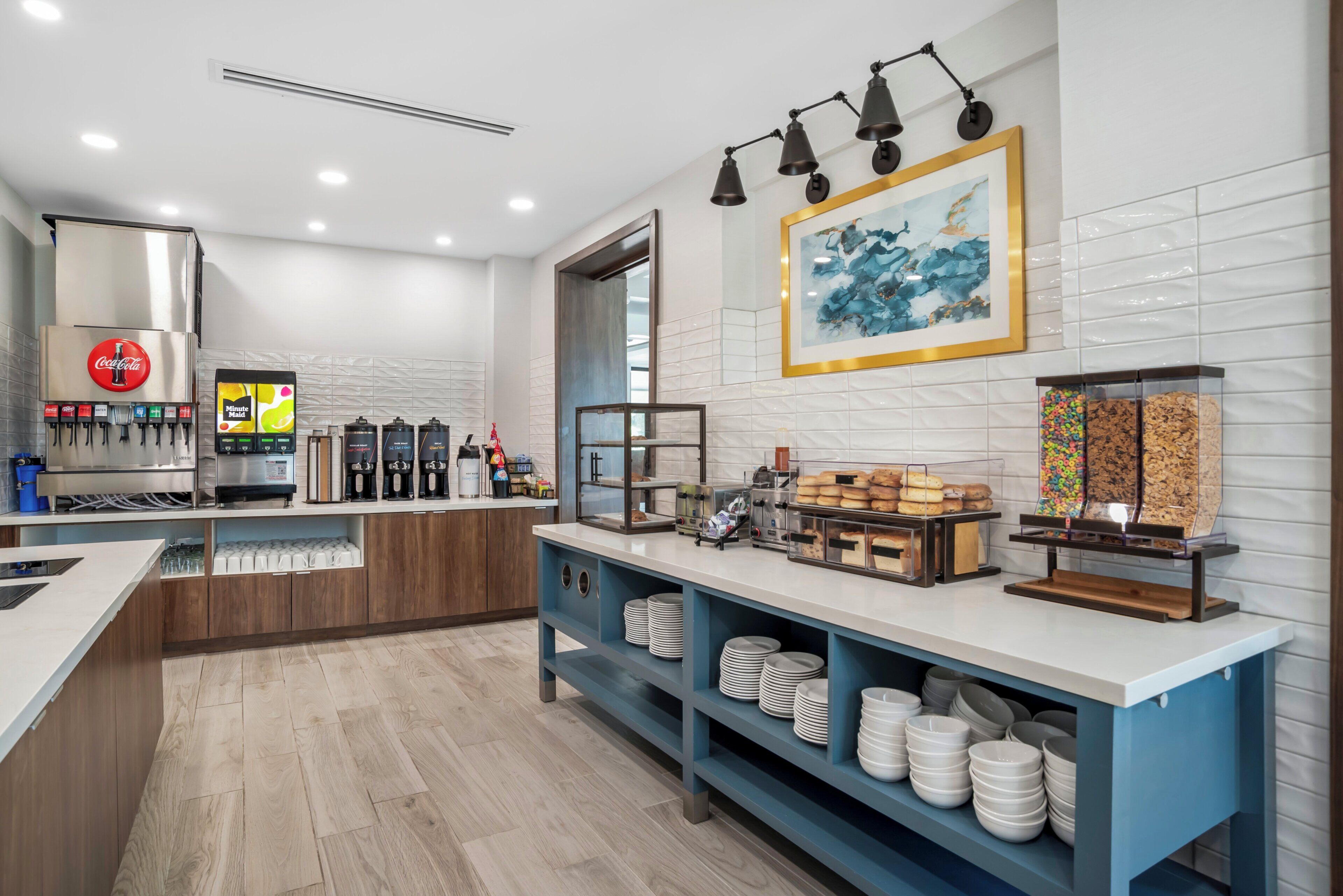 A modern kitchen with a coffee station, a refrigerator with beverage dispensers, and a counter with food items.