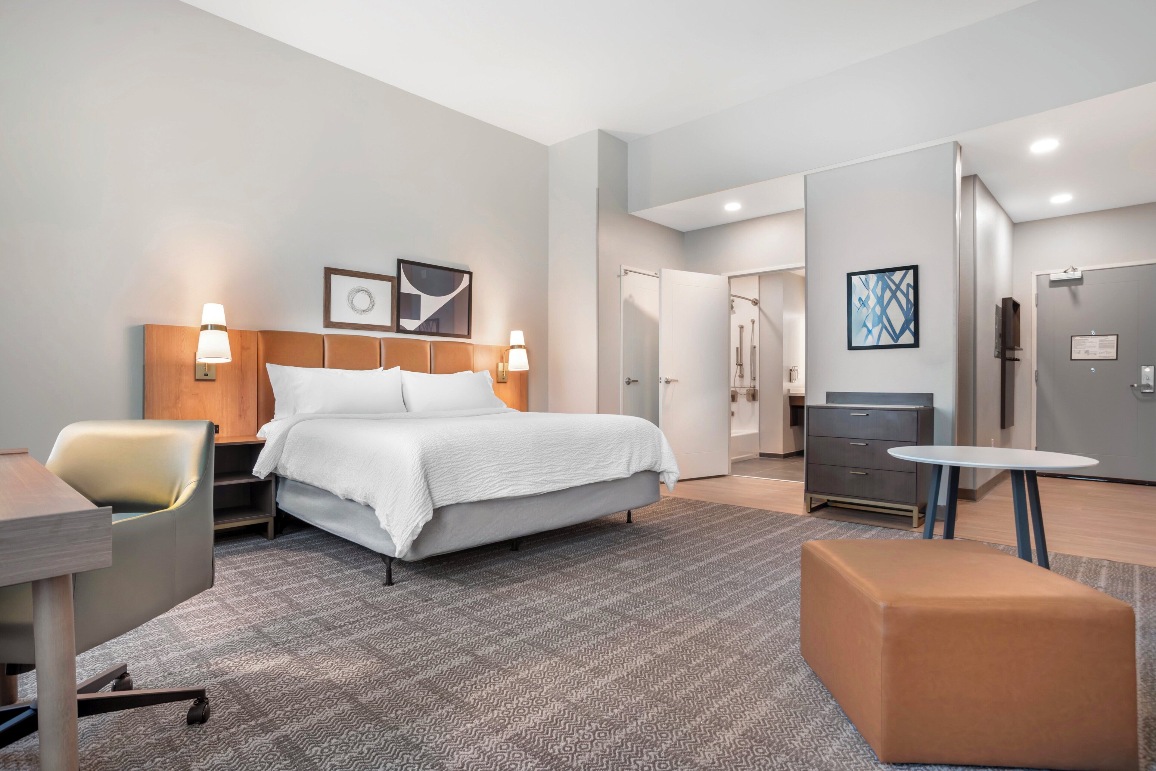 A hotel room with a bed, a desk, a chair, a small table, and a cabinet.