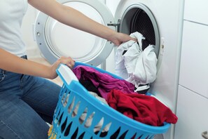 Una persona cargando una lavadora con una cesta de ropa.
