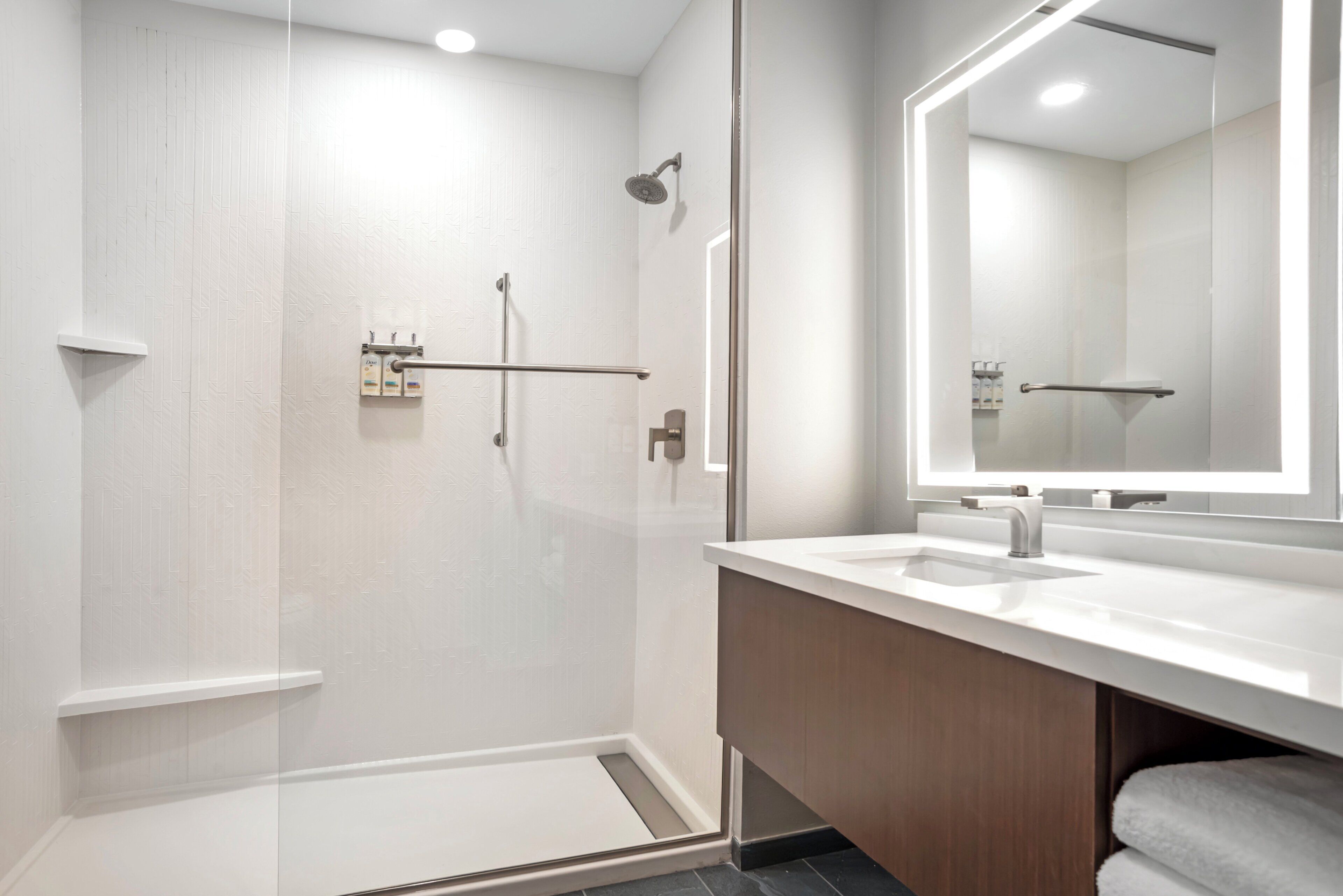 Un baño moderno con ducha a ras de suelo, un espejo grande y un tocador blanco.