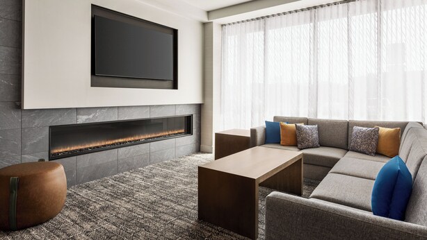 Una sala de estar moderna con un televisor de pantalla plana montado en la pared, una chimenea, un sofá modular con cojines y una mesa de centro.