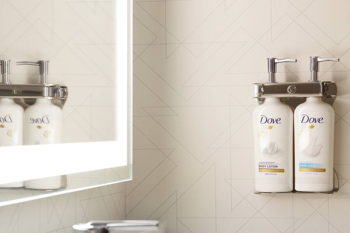 Une salle de bain dotée d’un lavabo moderne, d’un robinet chromé et de deux distributeurs de savon pour les mains de la marque Dove, fixés au mur.
