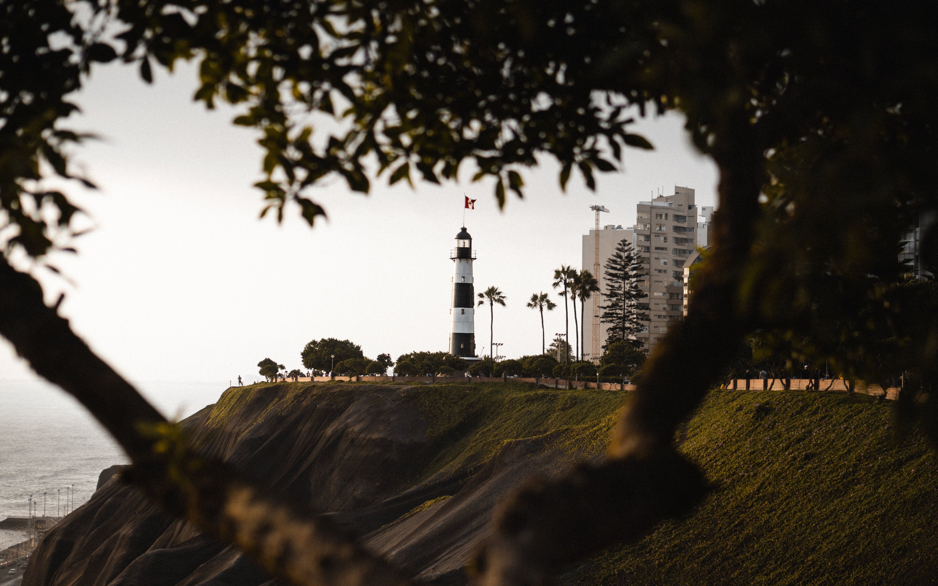 A lighthouse on a cliff with a view of the ocean and a cityscape in the background.