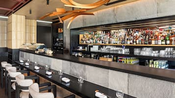 Zona de bar con una barra larga, diversas opciones de asientos y una variedad de botellas y copas.