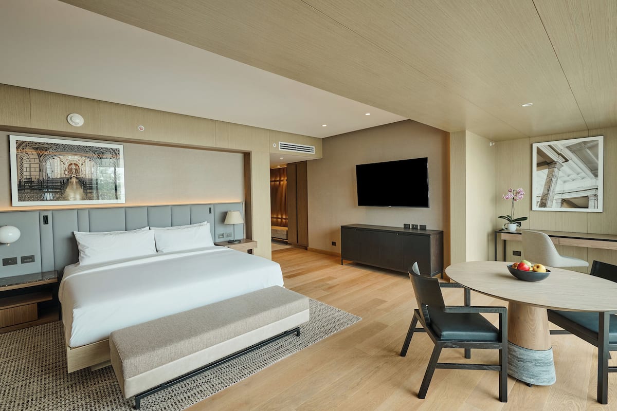 Una moderna camera d'albergo con un letto grande, un'area pranzo con un tavolo rotondo e una TV a schermo piatto montata a parete.