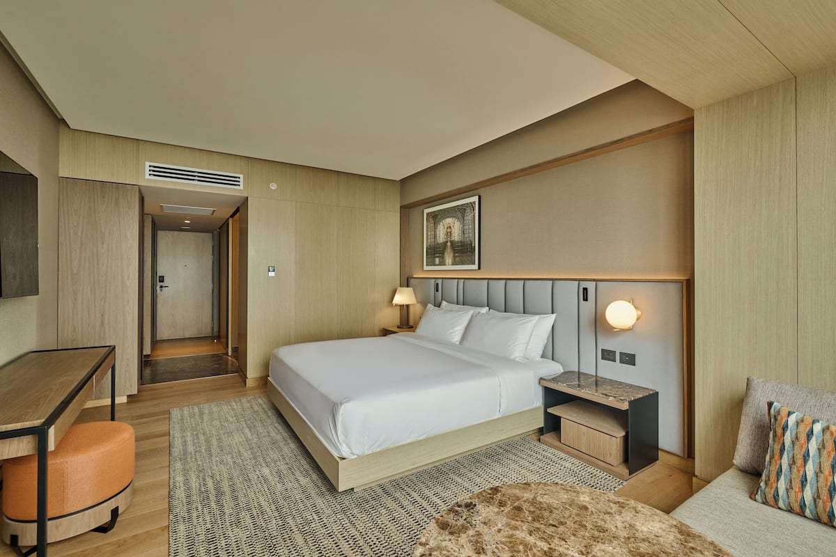 Una moderna camera d'hotel con un letto grande, una scrivania e una sedia. C'è un comodino con una lampada accanto al letto.