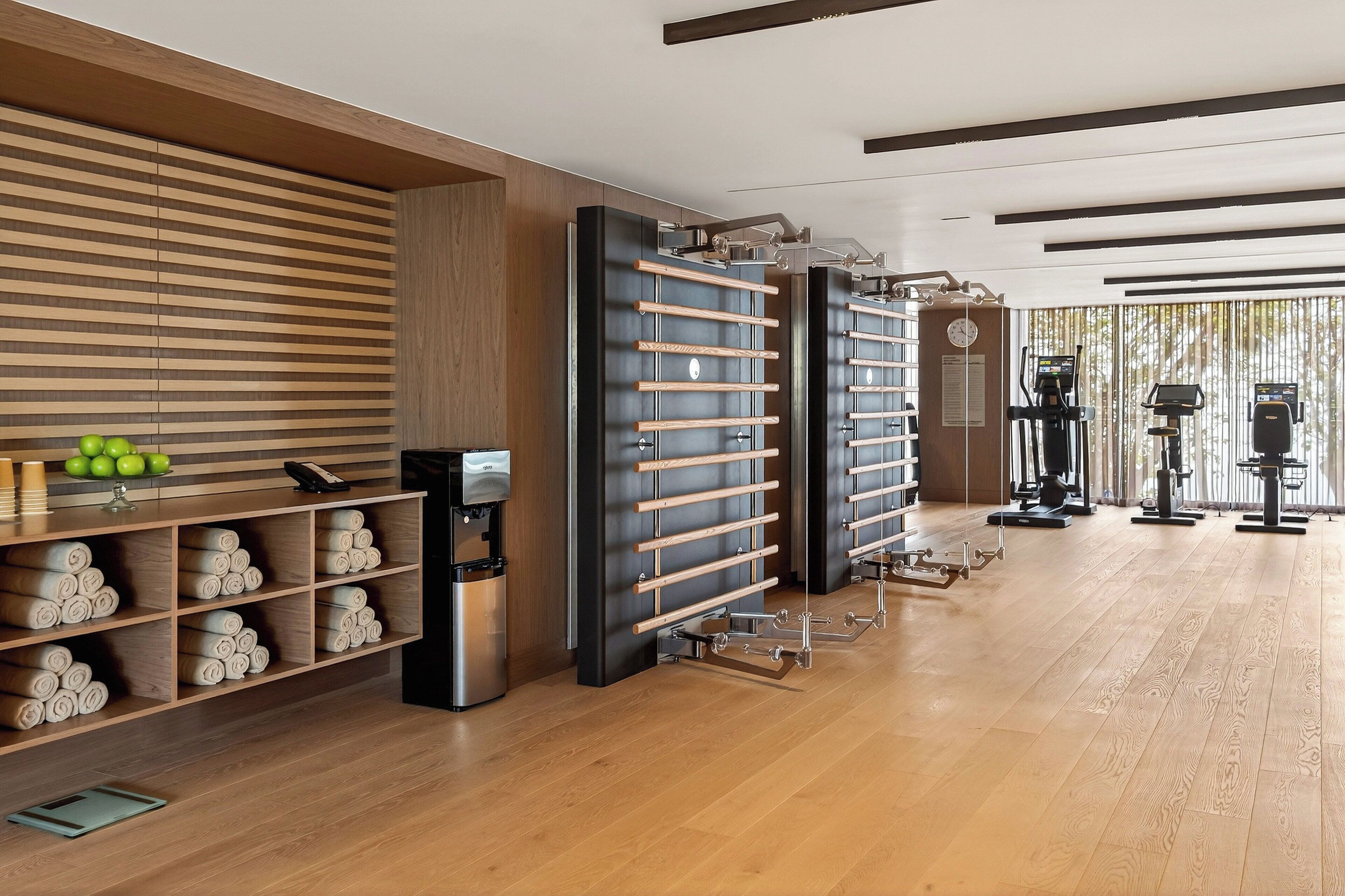 A modern gym with wooden floors, exercise equipment, and a towel rack.
