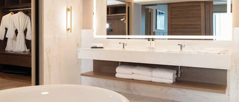 A modern bathroom with a large bathtub, a double sink vanity, and a walk-in closet with hanging robes.