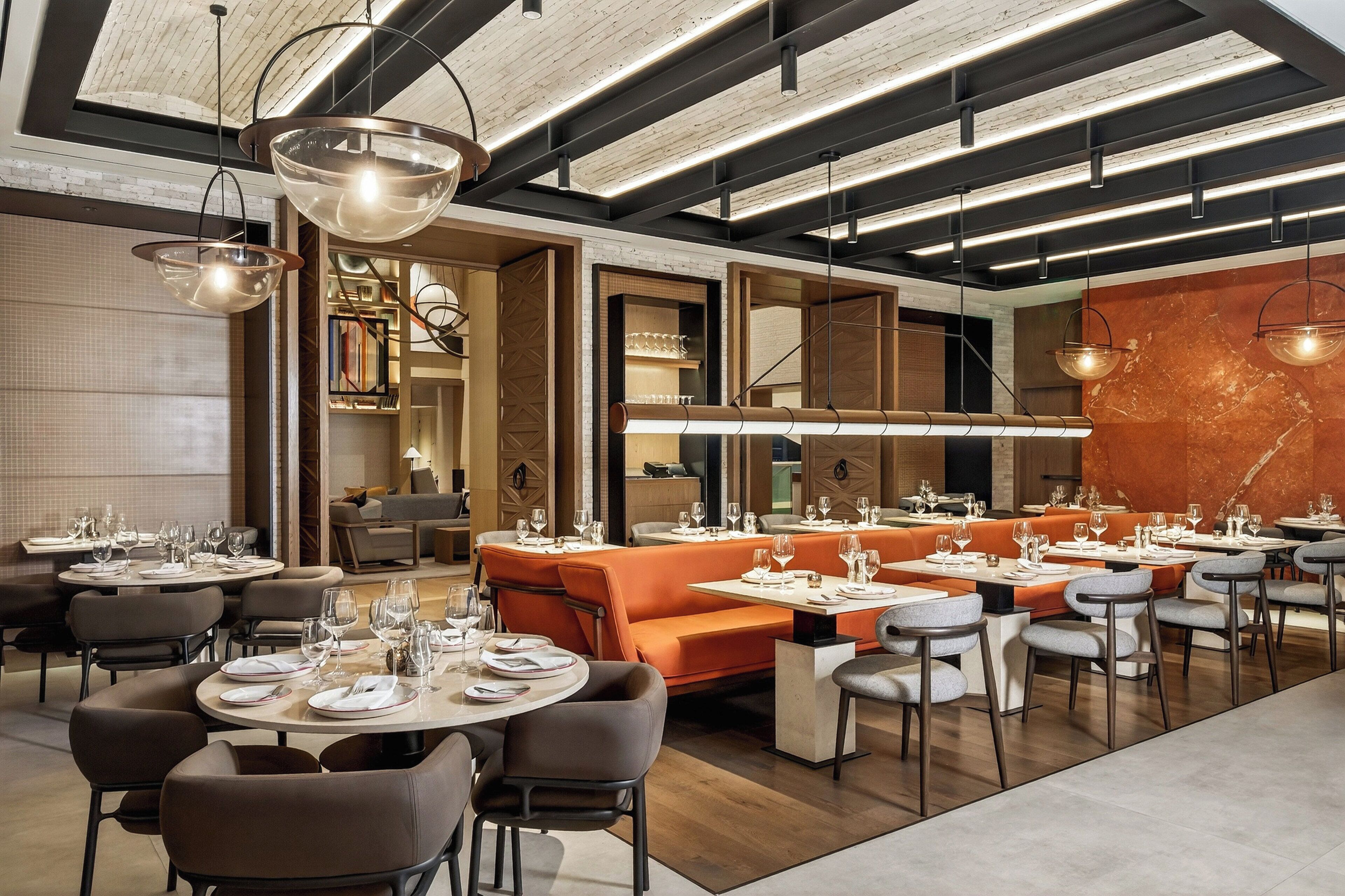 A modern restaurant with round tables, orange seating, and pendant lighting.