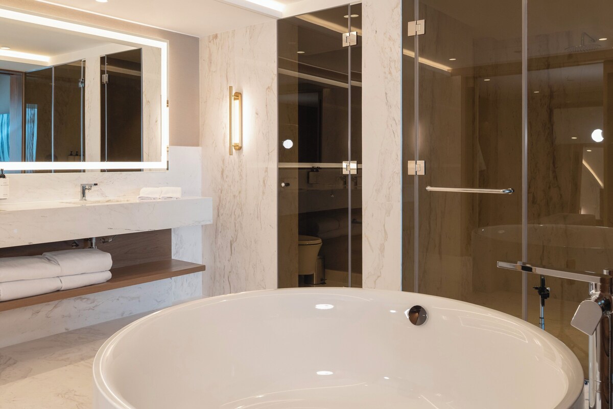 A modern bathroom with a large bathtub, a glass-enclosed shower, and a vanity with a mirror and towel rack.