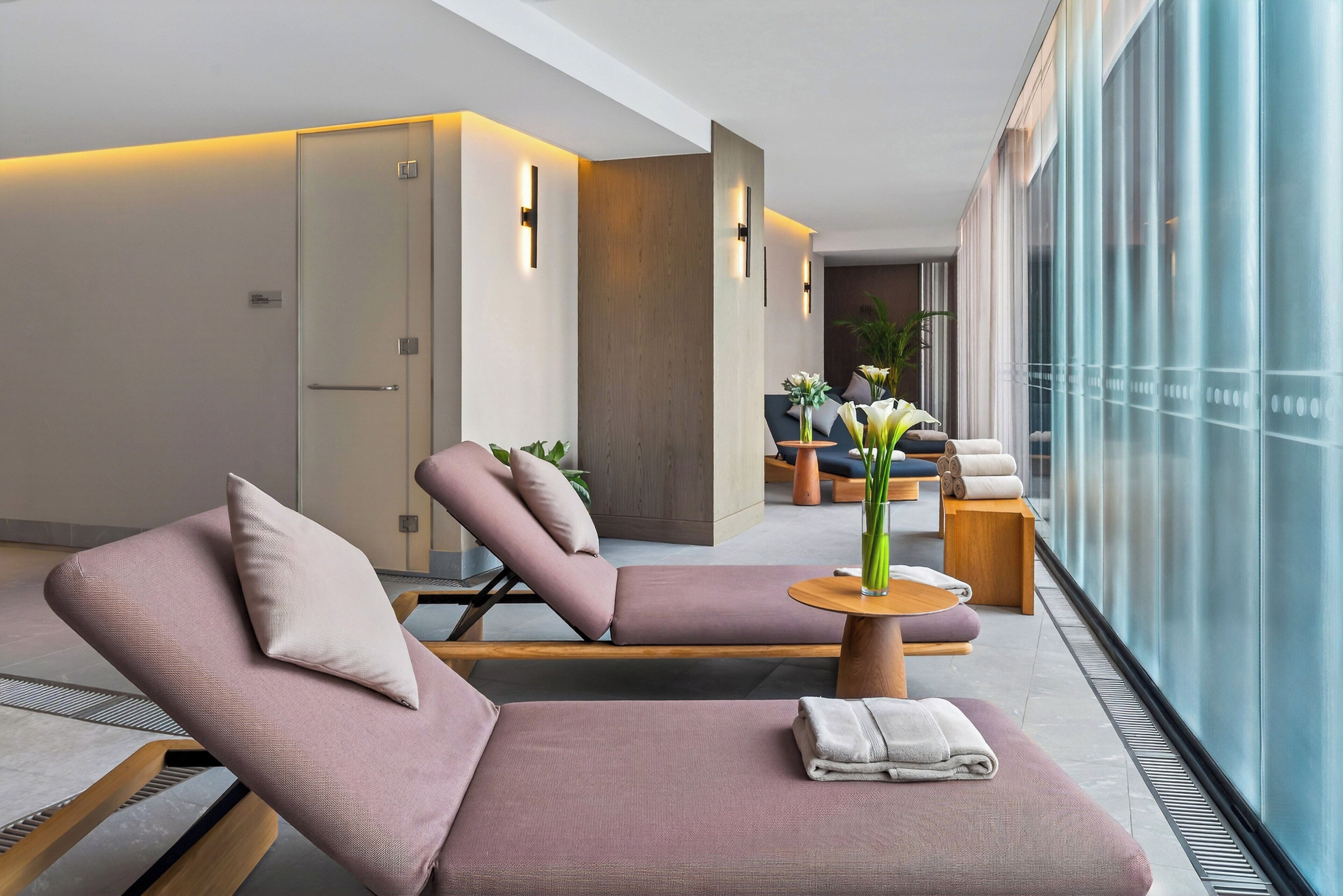 Un espace de détente moderne, doté de sièges confortables, d’une petite table avec un vase et offrant une vue à travers de grandes fenêtres en verre.