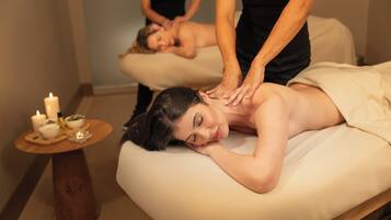 Une salle de massage équipée d’une table de massage, de bougies et d’une petite table en bois sur laquelle sont posés des bols et une bouteille.