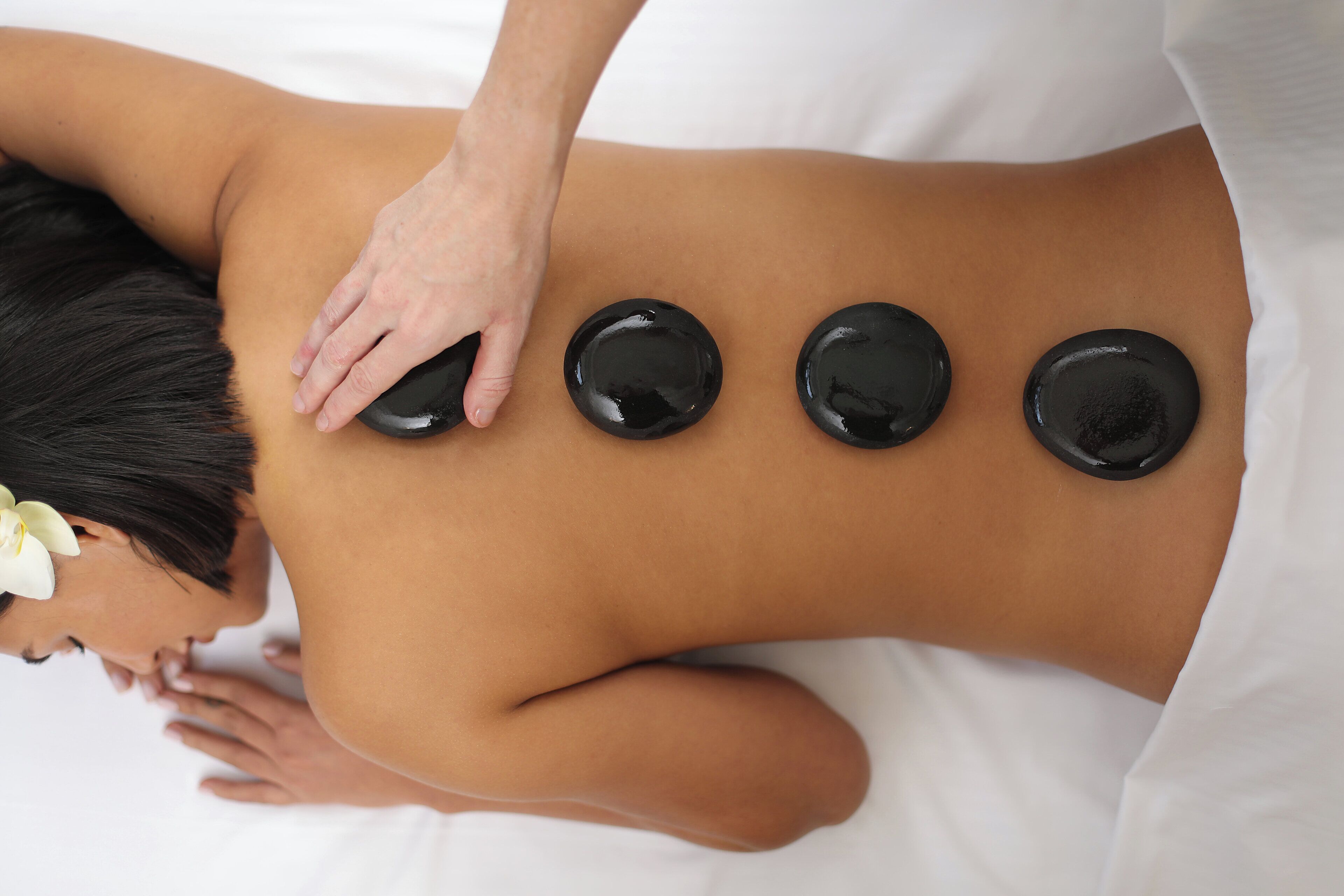 A person receiving a back massage with four hot stones placed on their back.