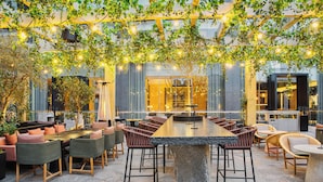 An outdoor dining area with a large stone table surrounded by wicker chairs, under a canopy of greenery and string lights. - InterContinental Real Lima Miraflores by IHG (Lima)