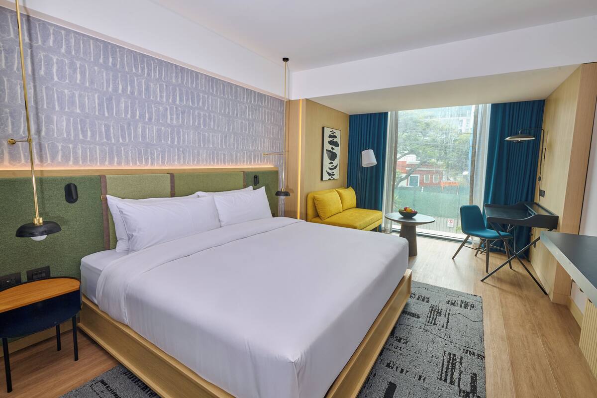 A hotel room with a large bed, a desk, a chair, and a view of the outdoors.