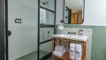 Un baño con un lavamanos blanco, toallero de madera y un espejo.