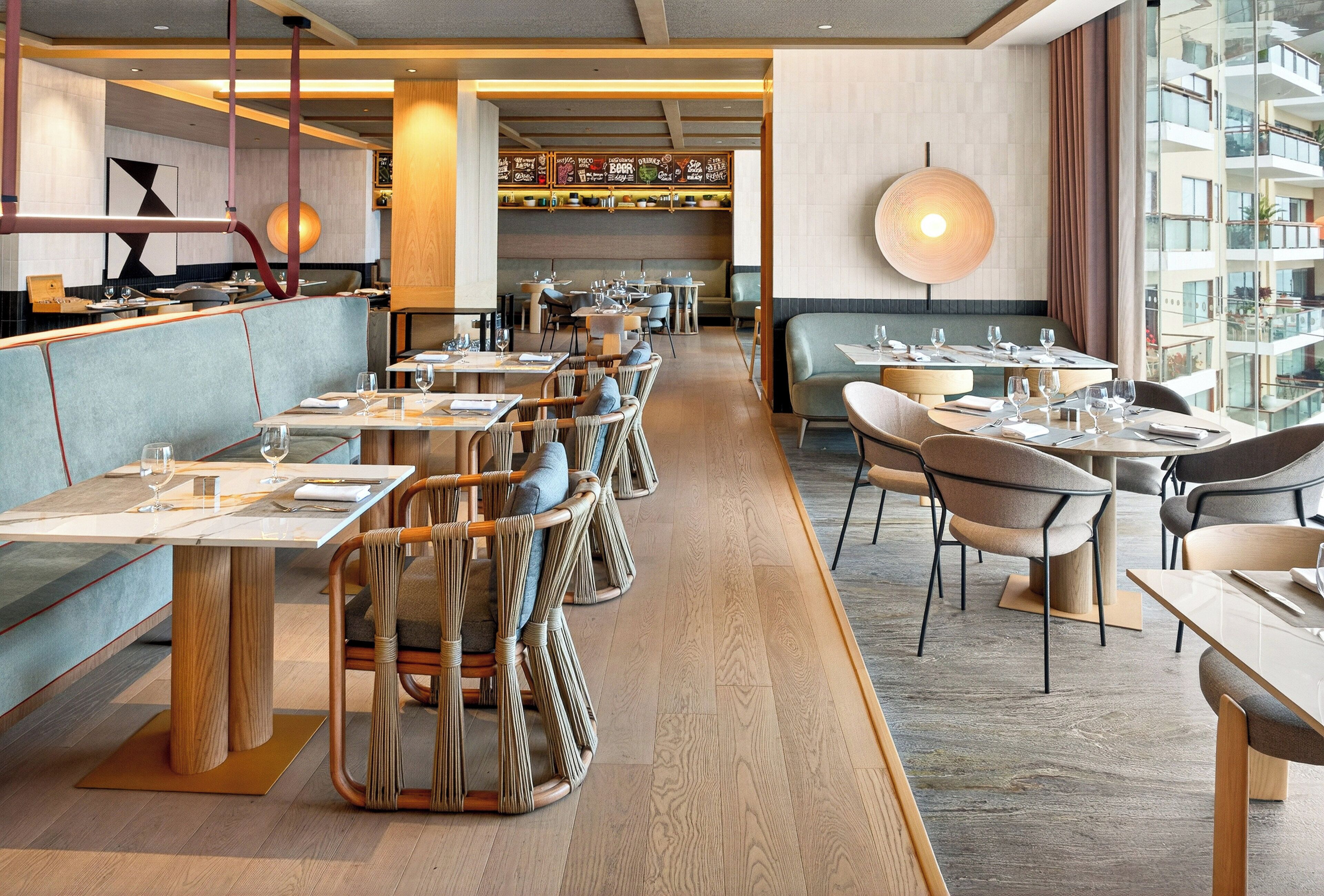A modern restaurant with wooden flooring, cushioned seating, and a variety of table settings.