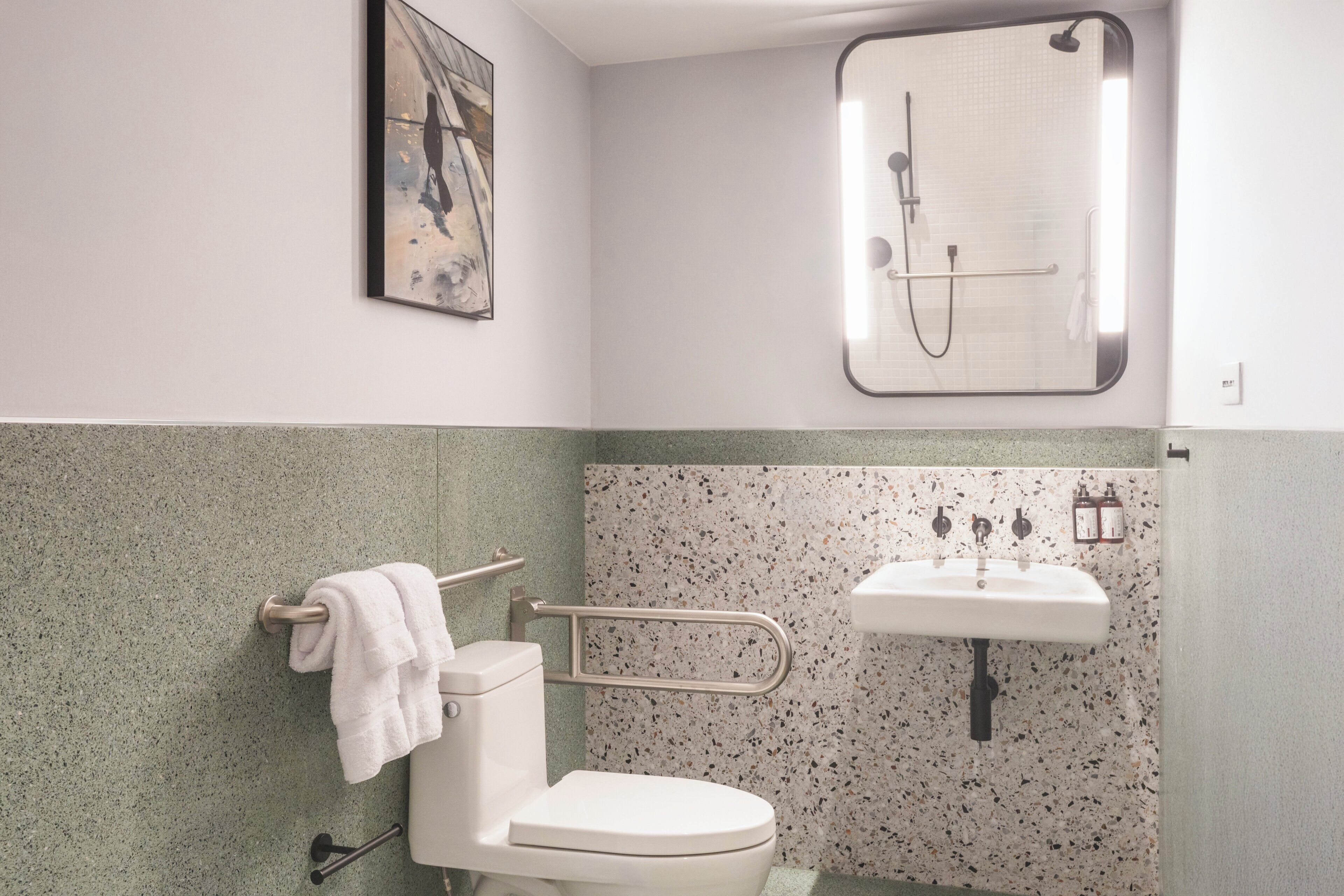A bathroom with a toilet, a handrail, a sink, and a shower enclosure.