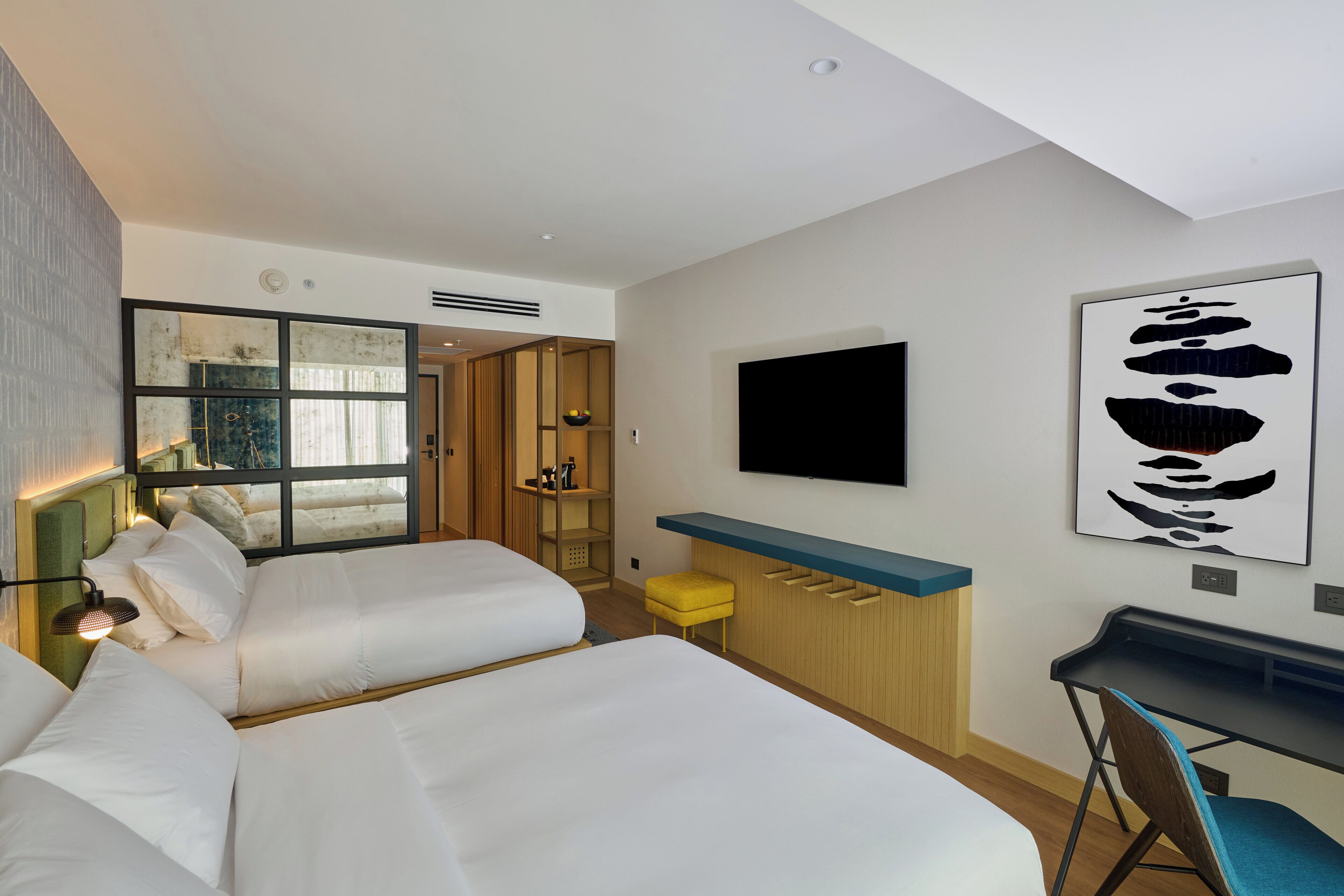A modern hotel room with two beds, a desk, a TV, and a large window.