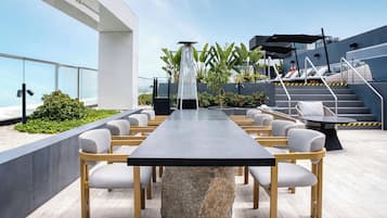 Terraza en la azotea con una mesa larga y sillas, rodeada de plantas y una escalera.