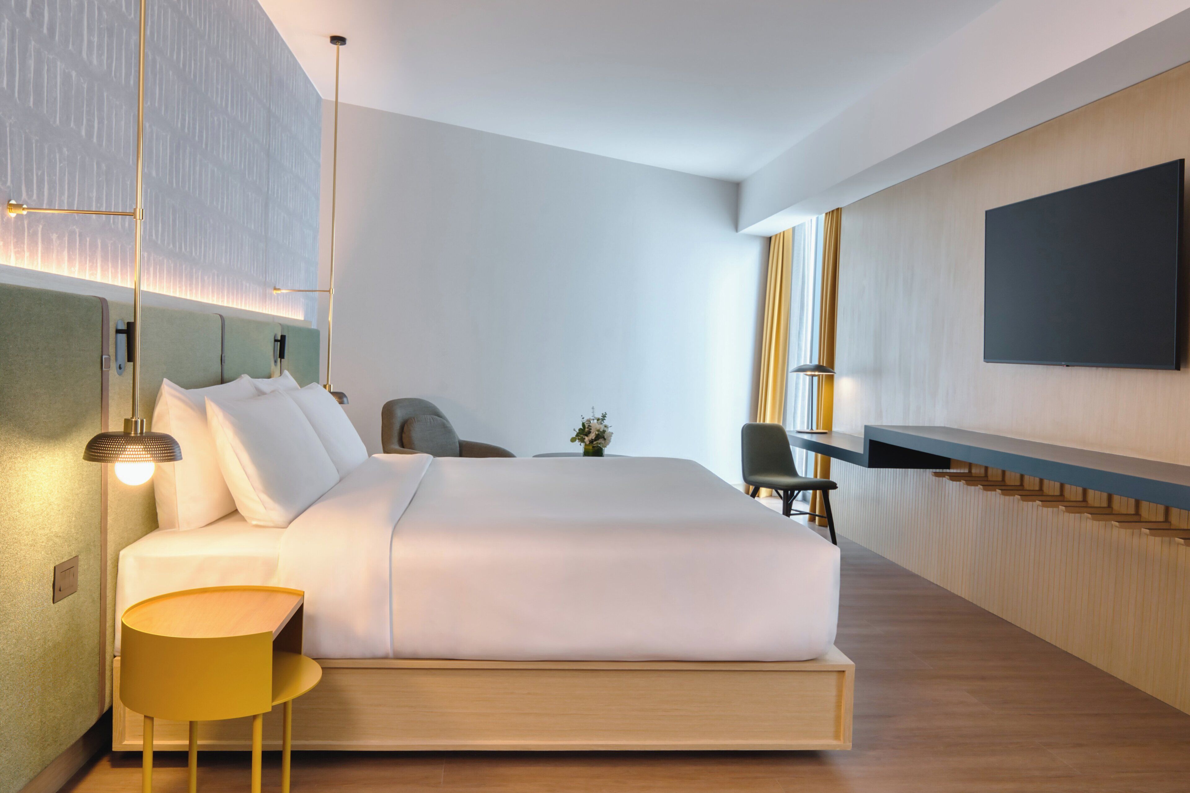 A modern hotel room with a large bed, a desk, and a flat-screen TV mounted on the wall.