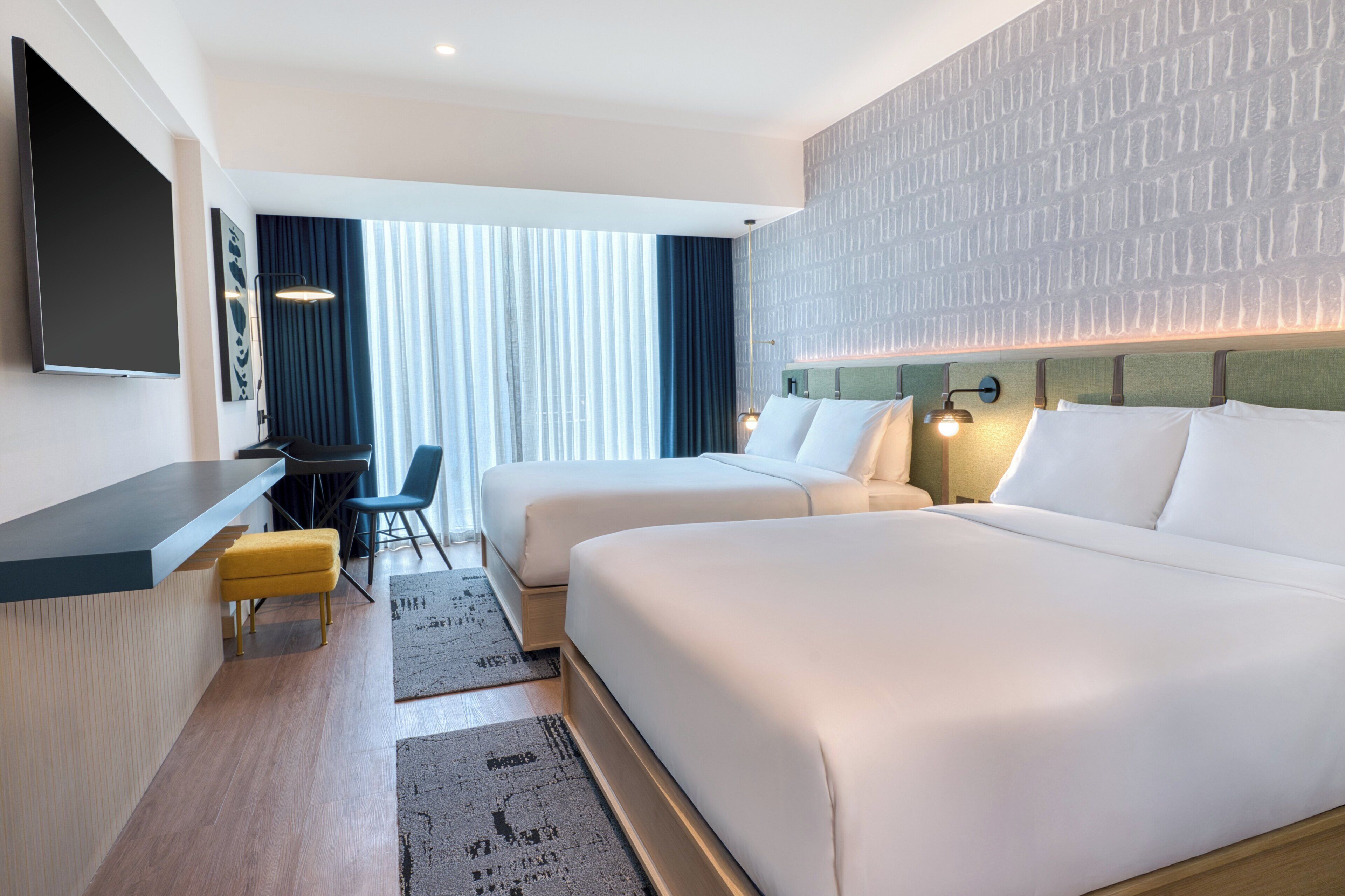 Habitación de hotel con dos camas, un escritorio, una silla y un televisor.