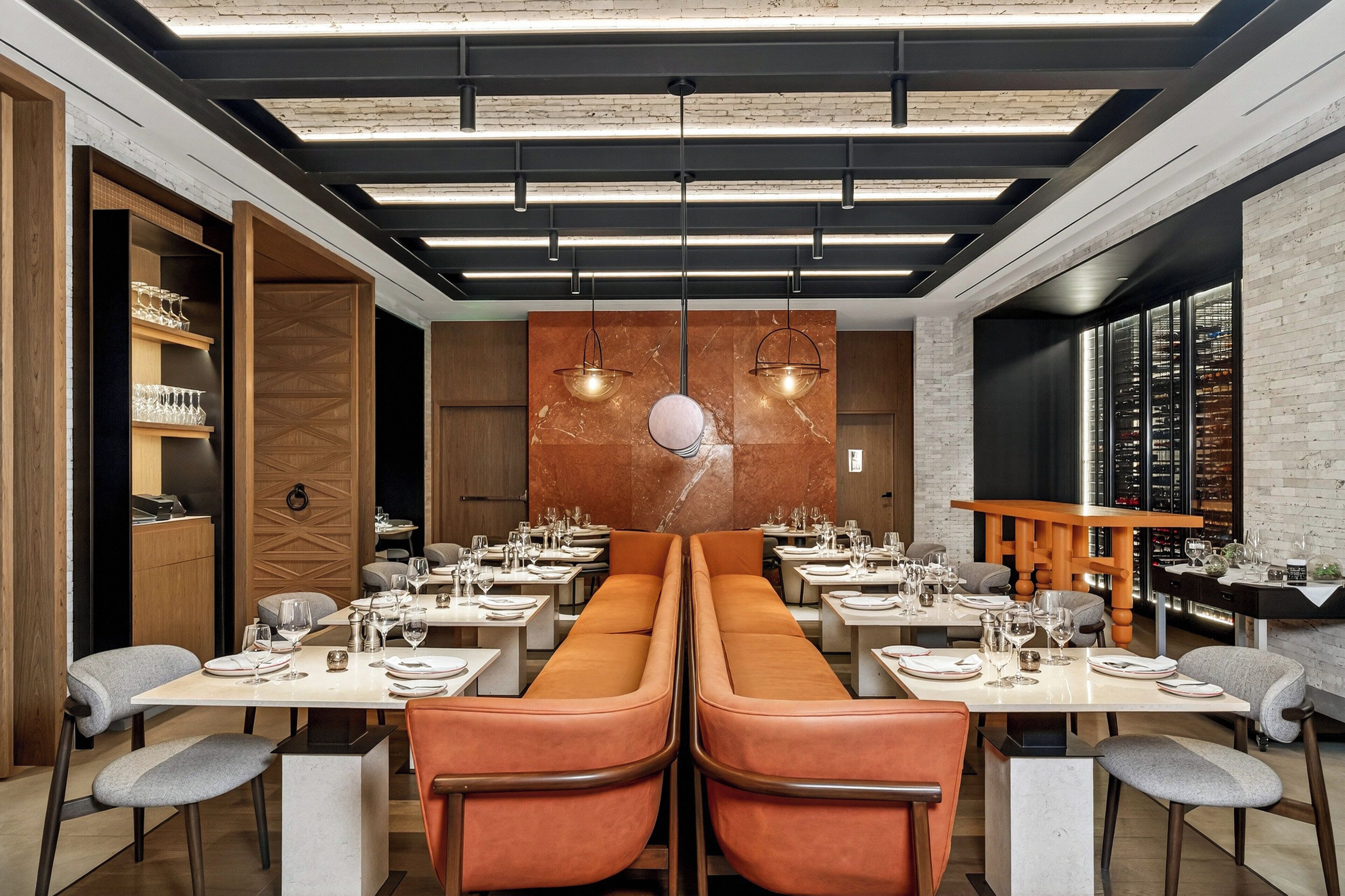 A modern restaurant with a long communal table, individual tables, and a wine rack.