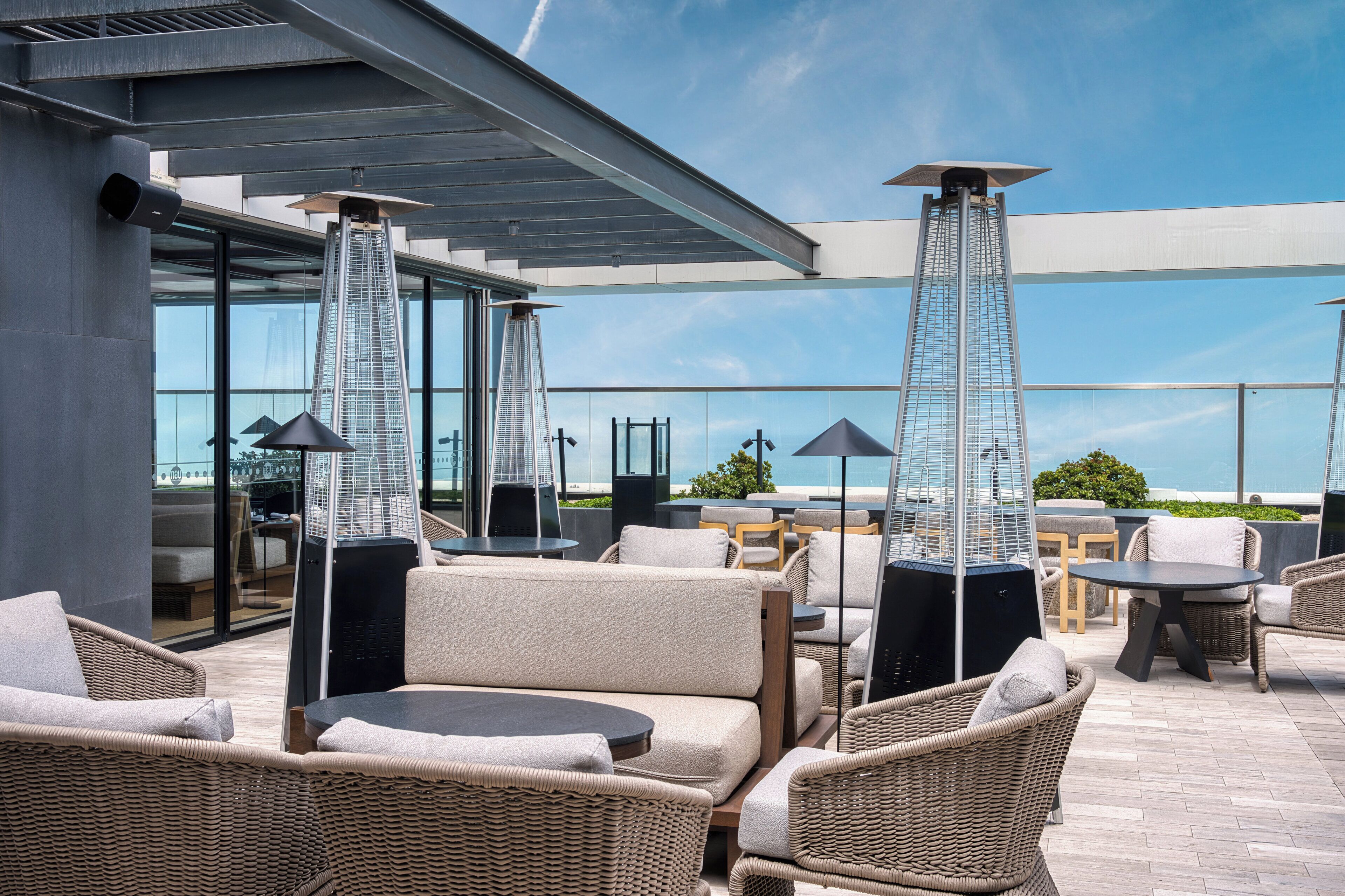An outdoor seating area with wicker furniture, a glass enclosure, and a view of a tall building.