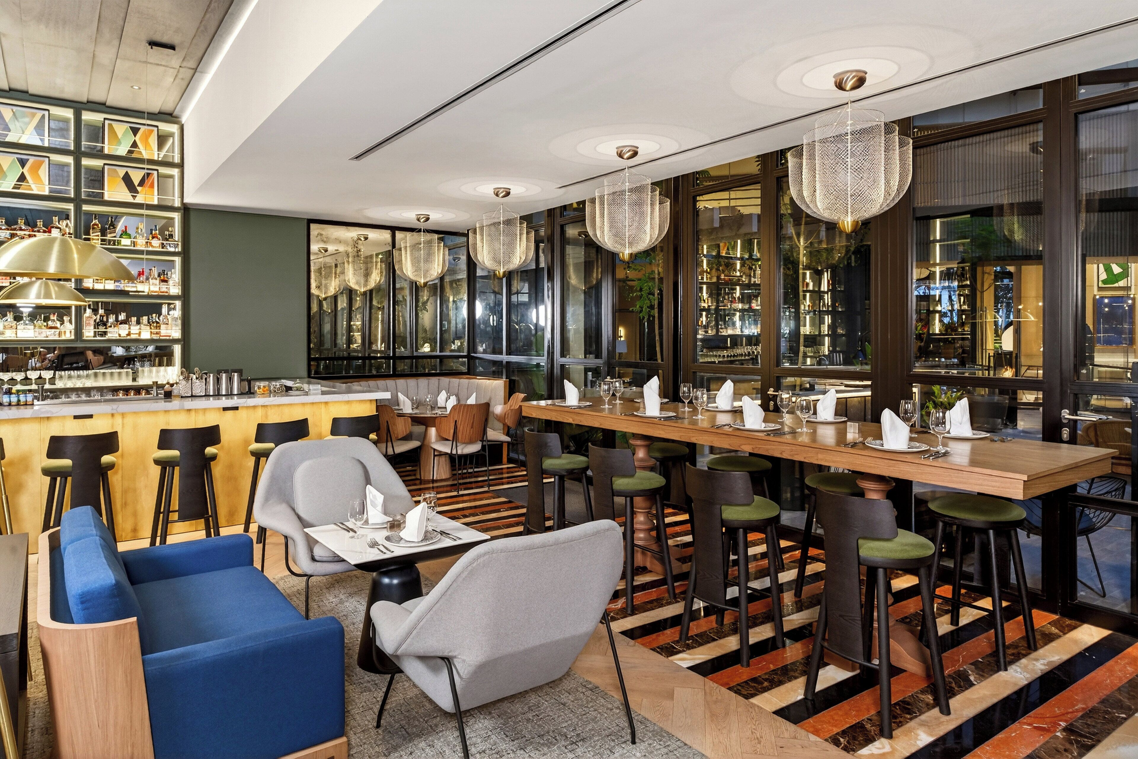 A modern bar area with a long counter, multiple stools, and a seating area with sofas and chairs.