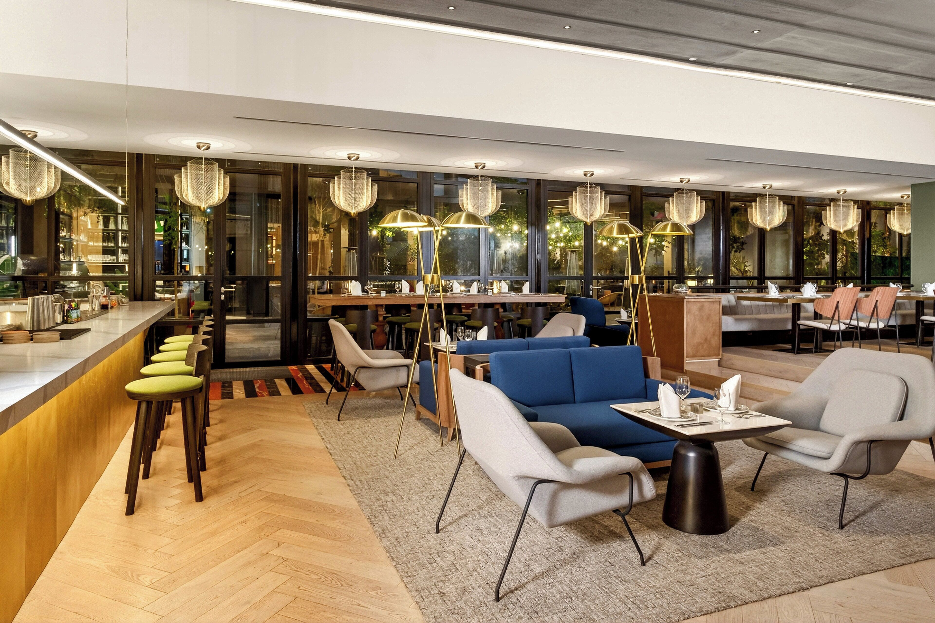 A modern restaurant with a bar area, seating with a mix of chairs and sofas, and decorative lighting.