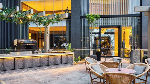 An outdoor patio area with wicker furniture, a bar with a grill, and a view of the interior through large windows. - Hotel Indigo Lima Miraflores by IHG (Lima)