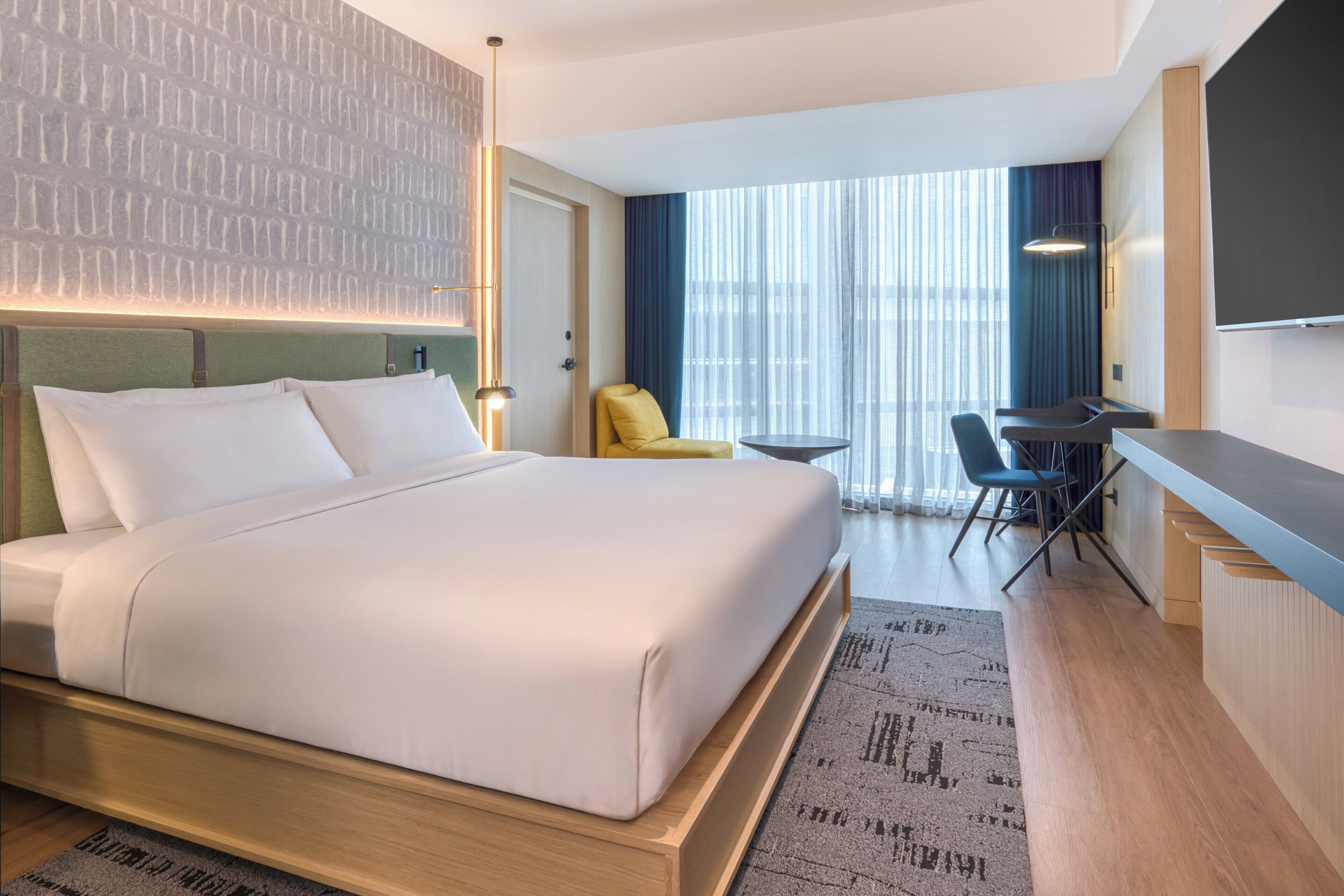 A hotel room with a large bed, a desk, a chair, a small table, and a TV.