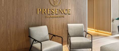 Interieur van een spa en wellnesscentrum, met een houten wand, twee grijze stoelen en een moderne lamp.