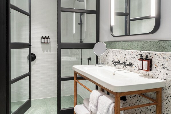 Un baño con lavamanos blanco, tocador de madera y cabina de ducha de vidrio.
