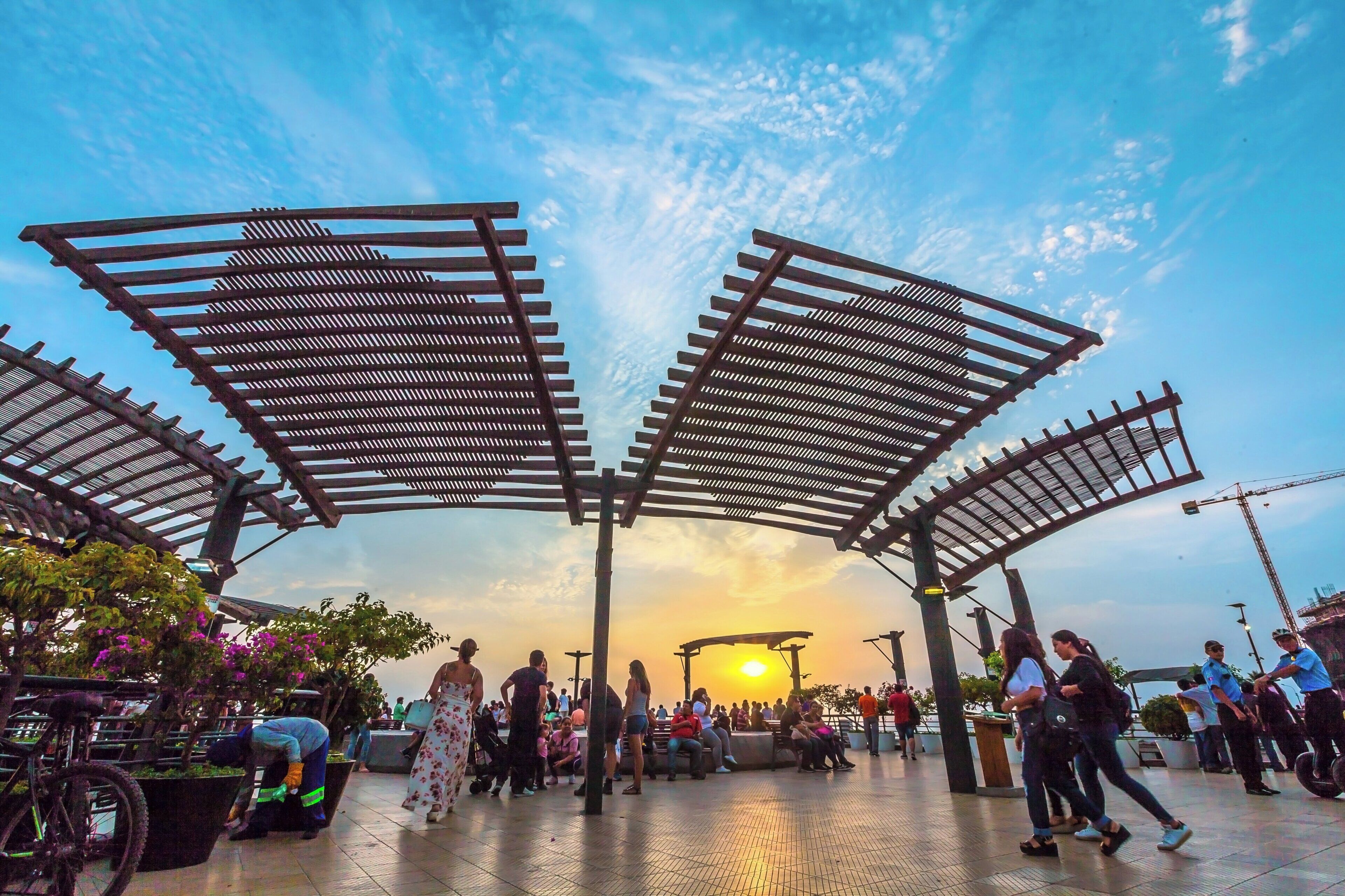 An outdoor public space with a canopy structure, seating areas, and people.