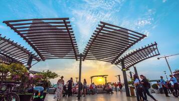 An outdoor public space with a canopy structure, seating areas, and people.