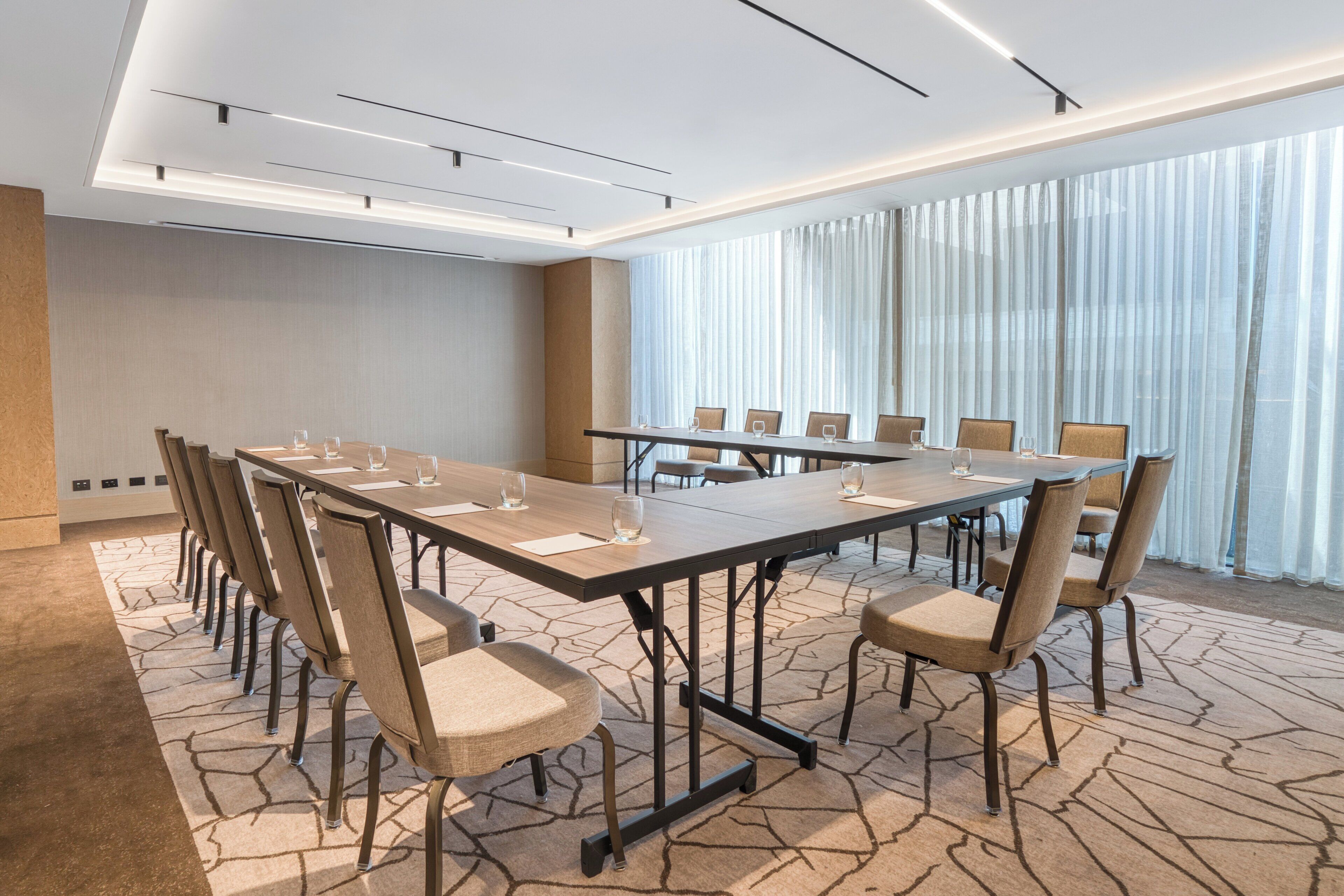 Un salón de conferencias con una larga mesa, varias sillas y un amplio ventanal con cortinas.