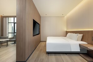 Une chambre d’hôtel moderne dotée d’un grand lit, d’un téléviseur à écran plat fixé au mur, d’un mur d’accent en bois et offrant une vue sur la ville par la fenêtre.