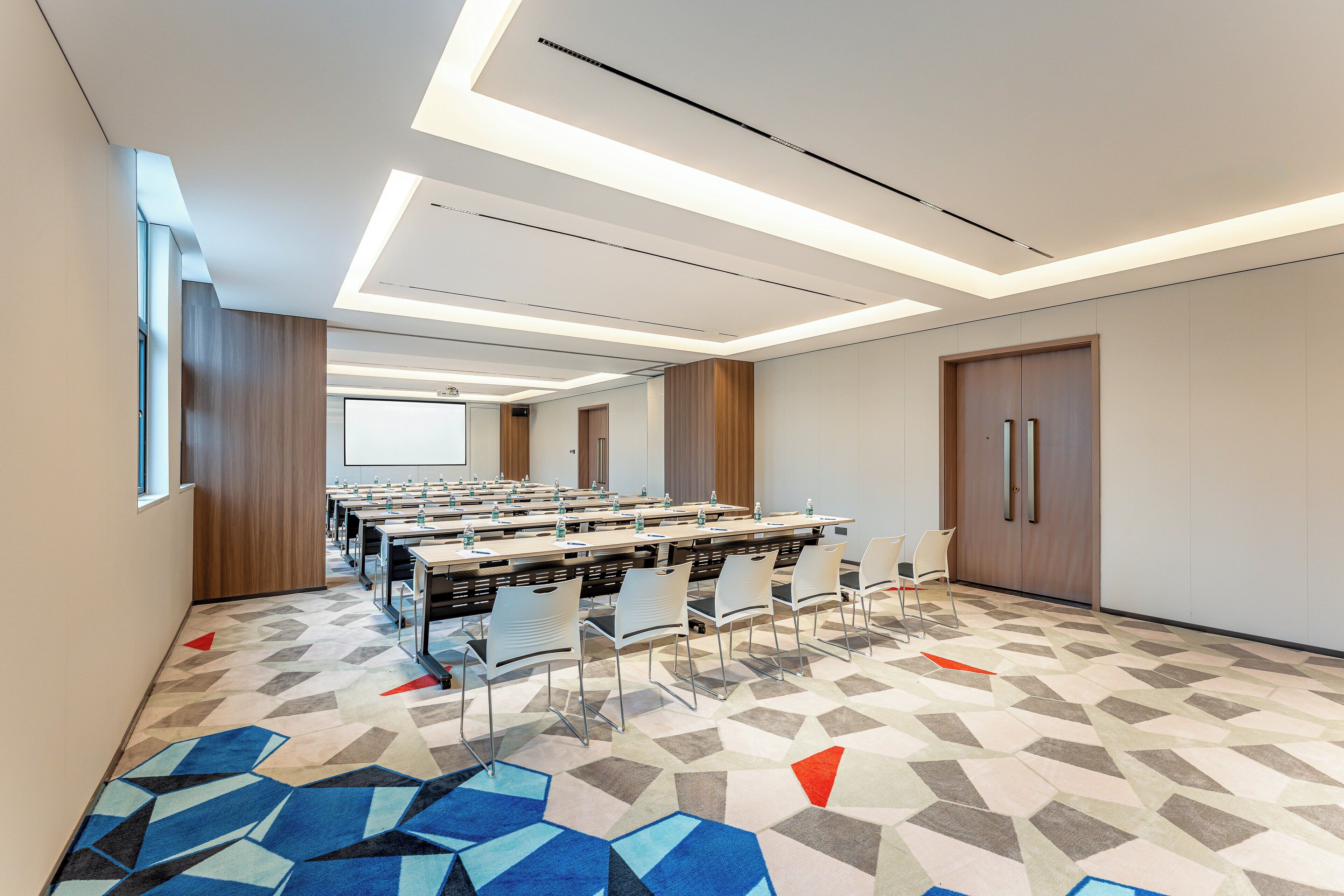 A conference room with long tables, chairs, and a projector screen.