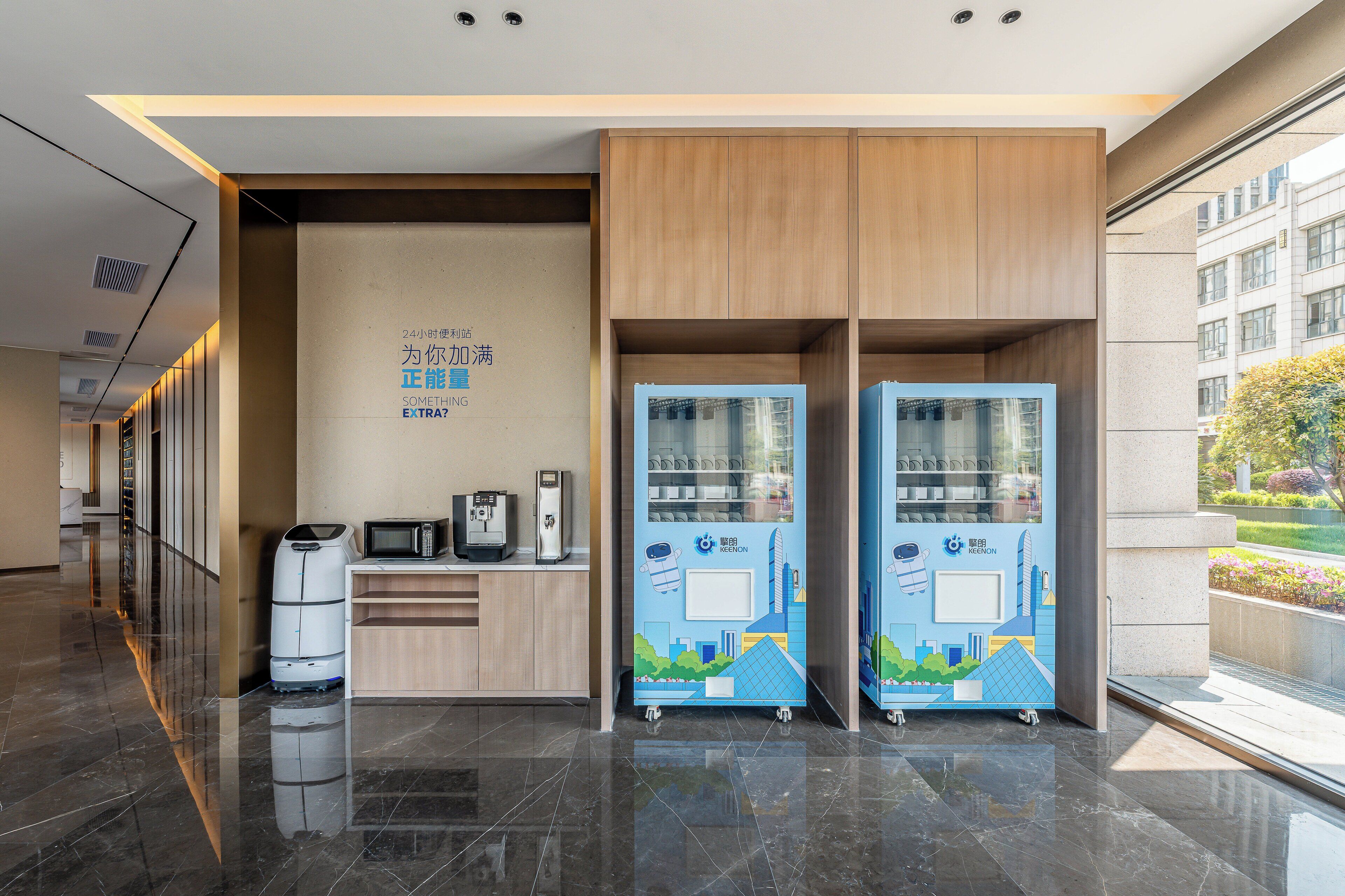 Un moderno vestíbulo de hotel con mostrador de recepción, máquinas expendedoras y vistas a la ciudad.