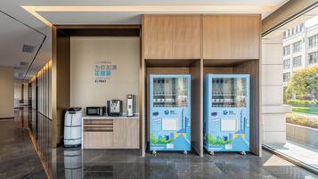 Un moderno vestíbulo de hotel con mostrador de recepción, máquinas expendedoras y vistas a la ciudad.