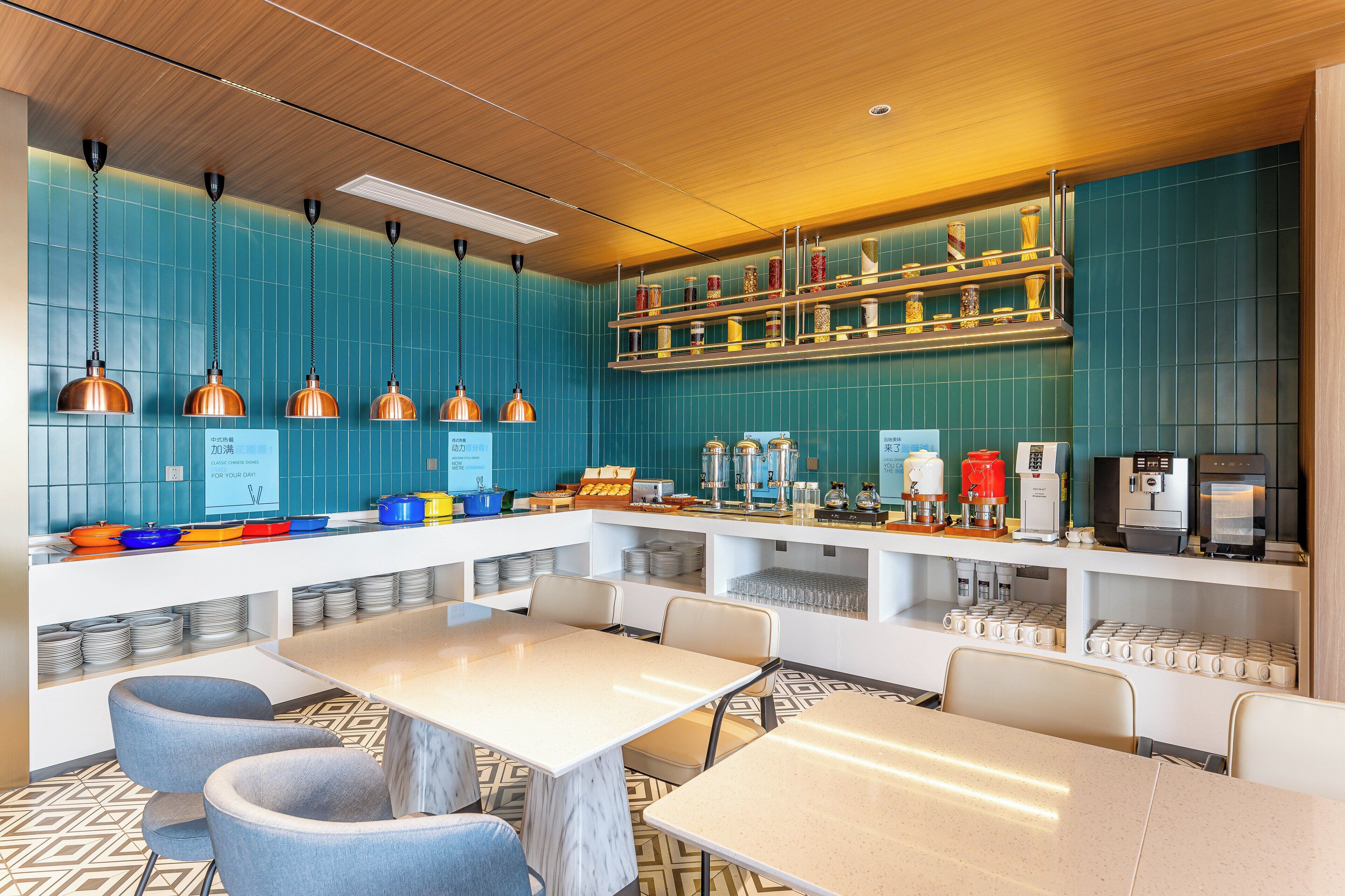 A modern restaurant with teal walls, copper pendant lights, and a variety of food and drink dispensers.