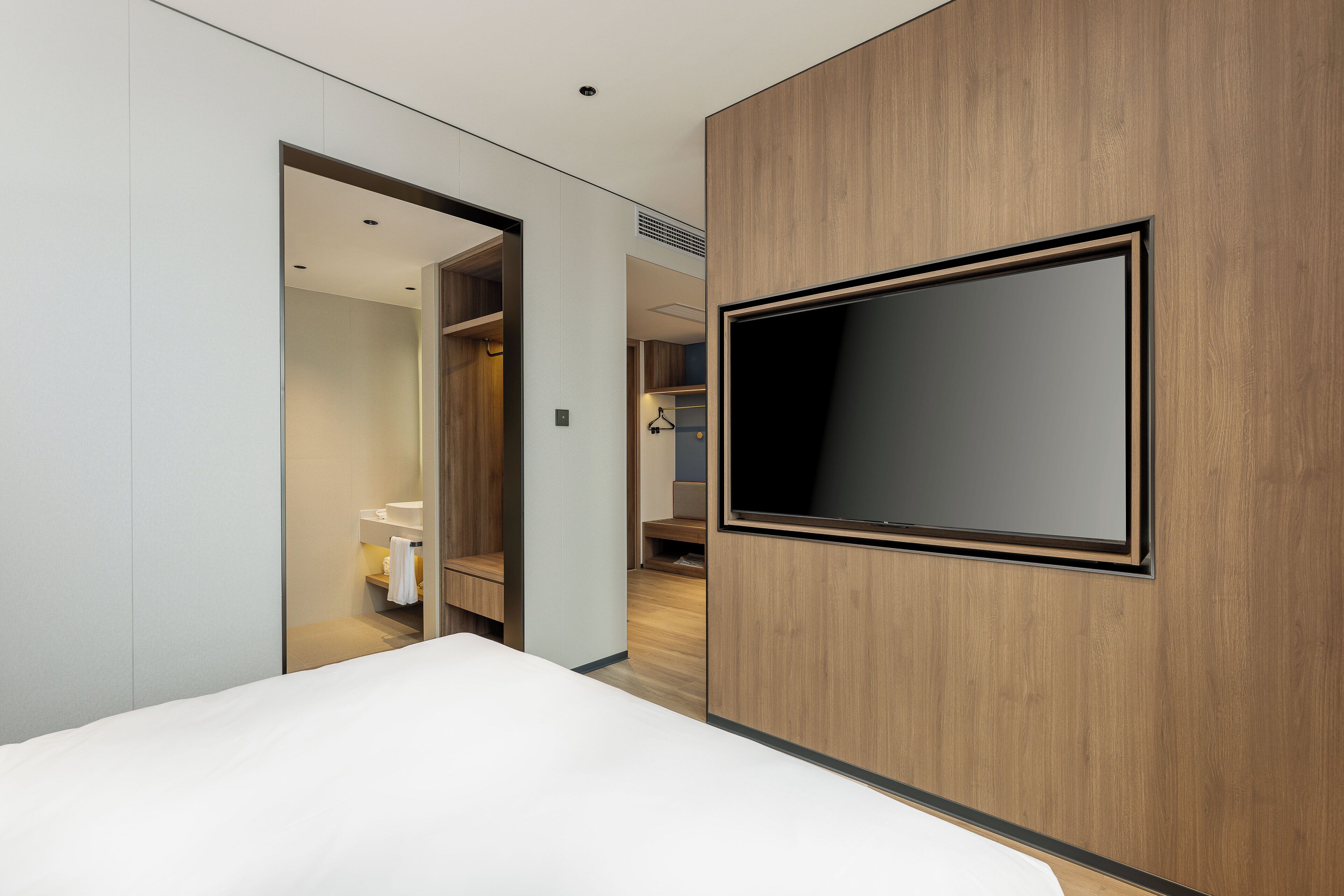 Ein modernes Hotelzimmer mit einem großen Bett, einem flachbildfernseher an der Wand und einem begehbaren Kleiderschrank.