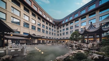 A hotel courtyard with a traditional pavilion, a hot spring, and a modern building with multiple windows.
