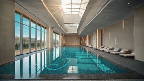 Ein Hallenbad mit Oberlichter, sonnendurchfluteter Decke und Liegestühlen am Rand.
