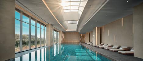 An indoor swimming pool with a skylight, sunlit ceiling, and lounge chairs along the side.