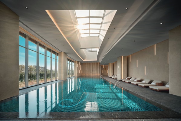 An indoor swimming pool with a skylight, sunlit ceiling, and lounge chairs along the side. - Holiday Inn Wuhan Tianhe Airport by IHG (Wuhan)