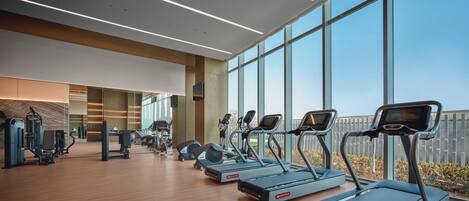 A modern gym with treadmills, weight machines, and large windows offering views of the outdoors.